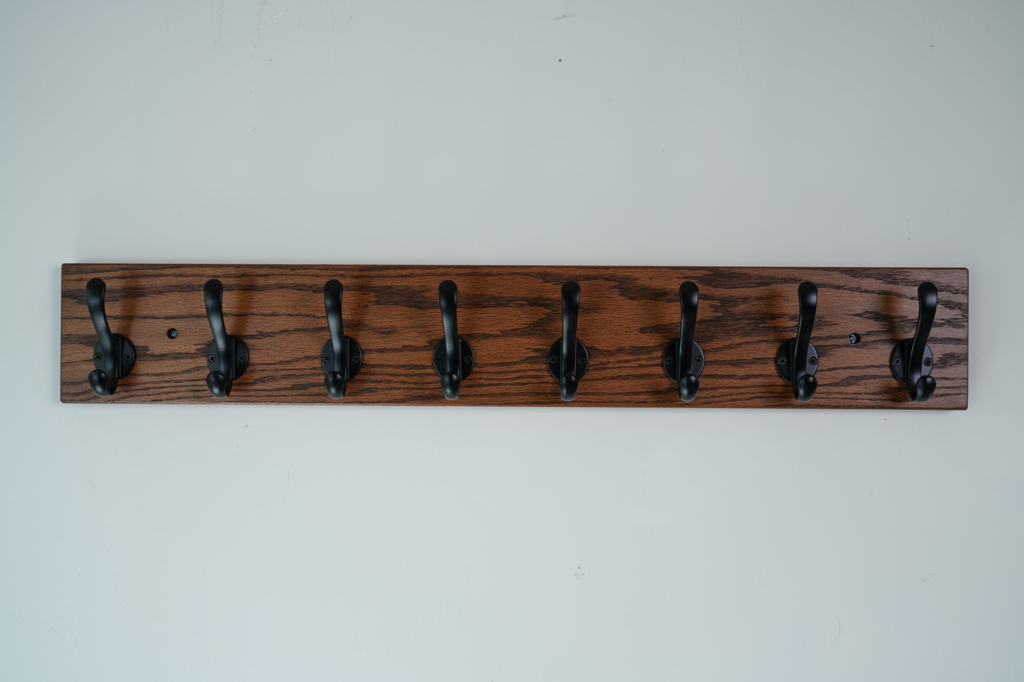 Wooden wall hook rack with six black hooks on a white background