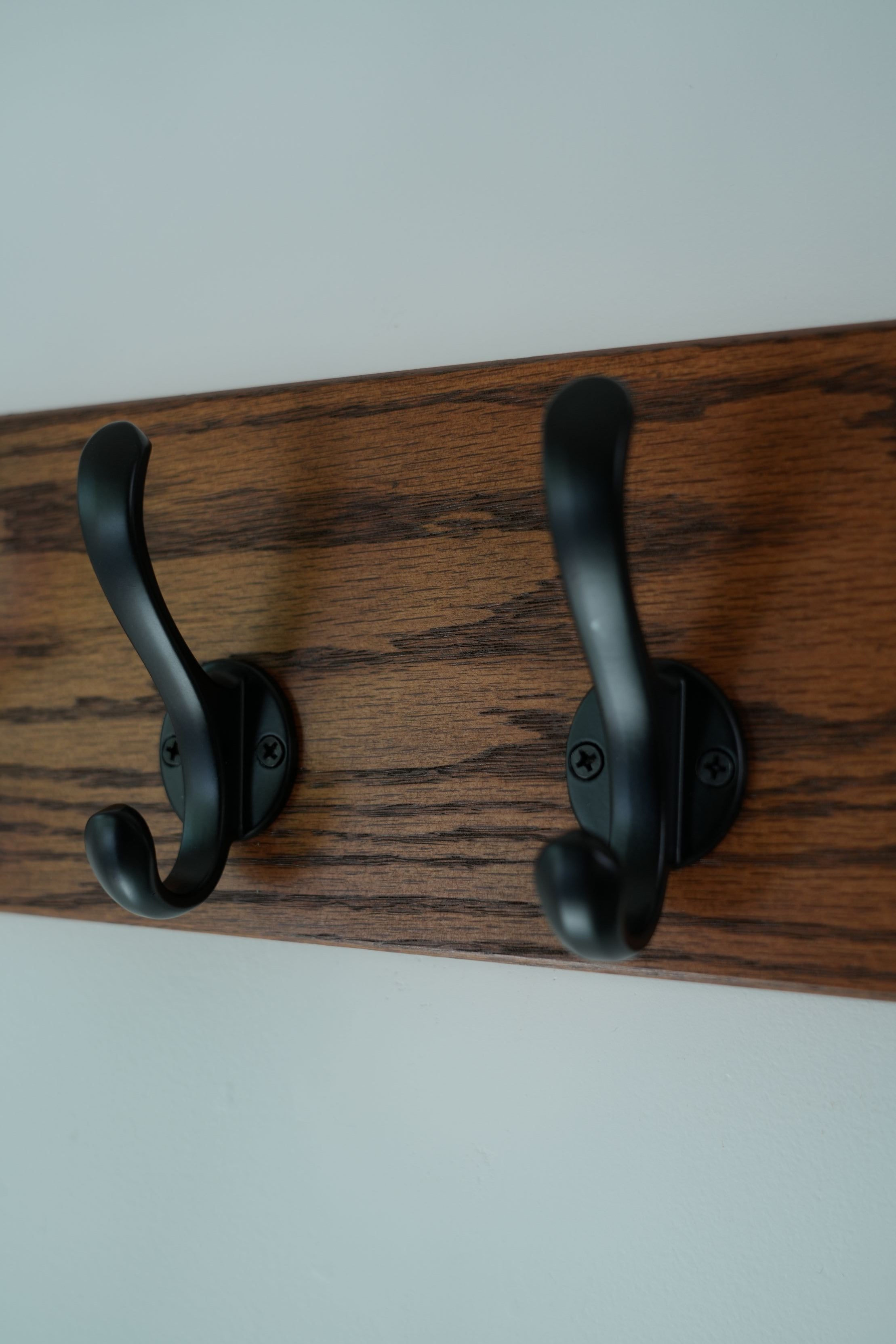 Two black coat hooks on a wooden board with a white background