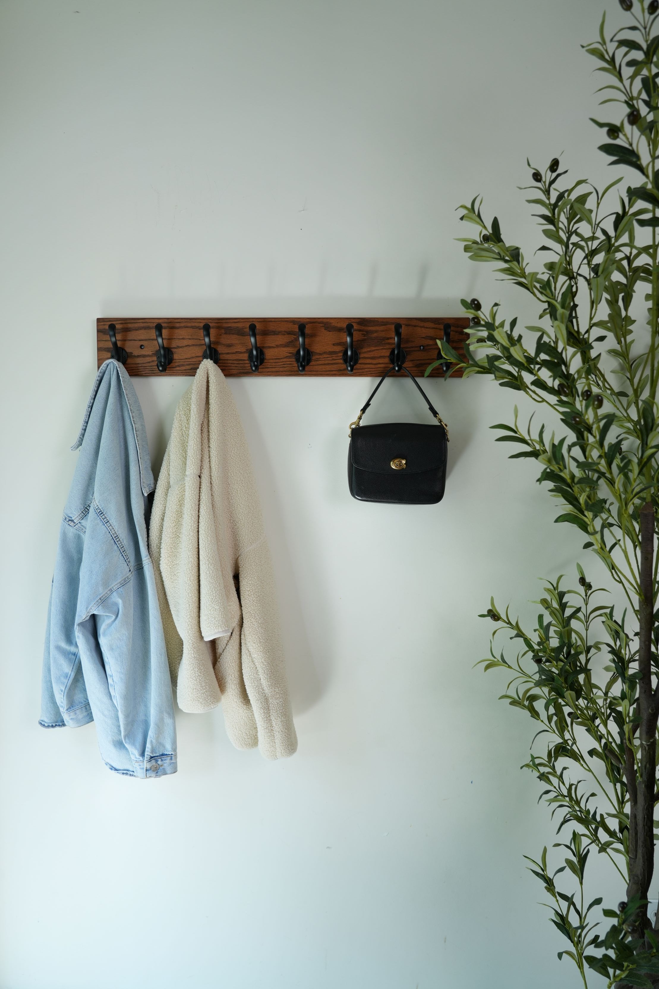 Wooden wall rack with folded clothes and a black handbag against a light background