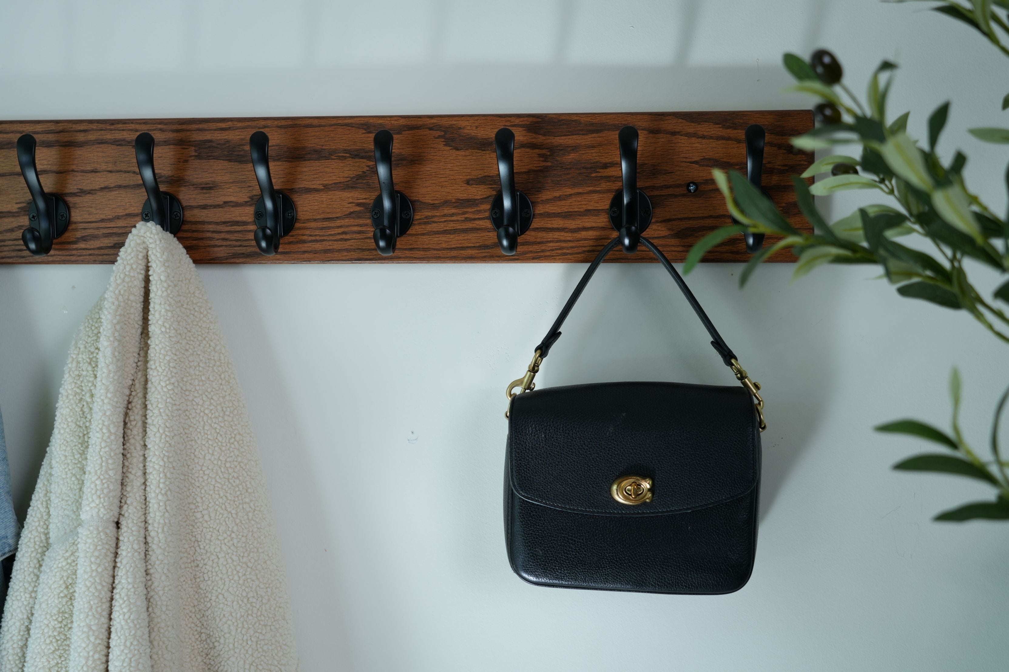 Black handbag hanging on a wooden hook rack with a white wall background
