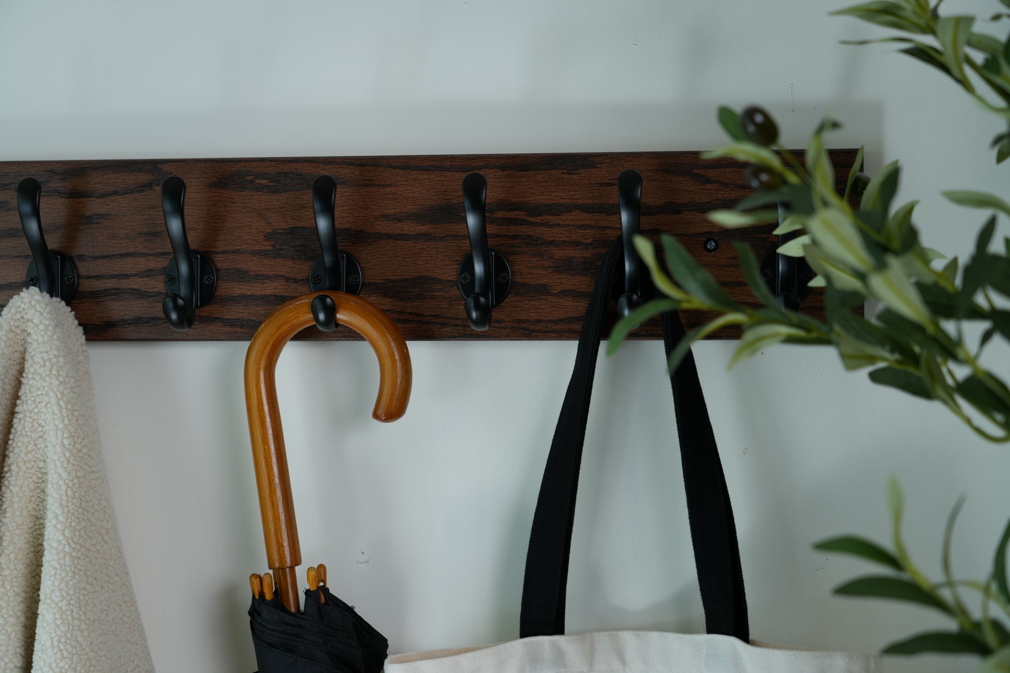 Wooden coat rack with hooks holding an umbrella, a belt, and a towel against a white wall.