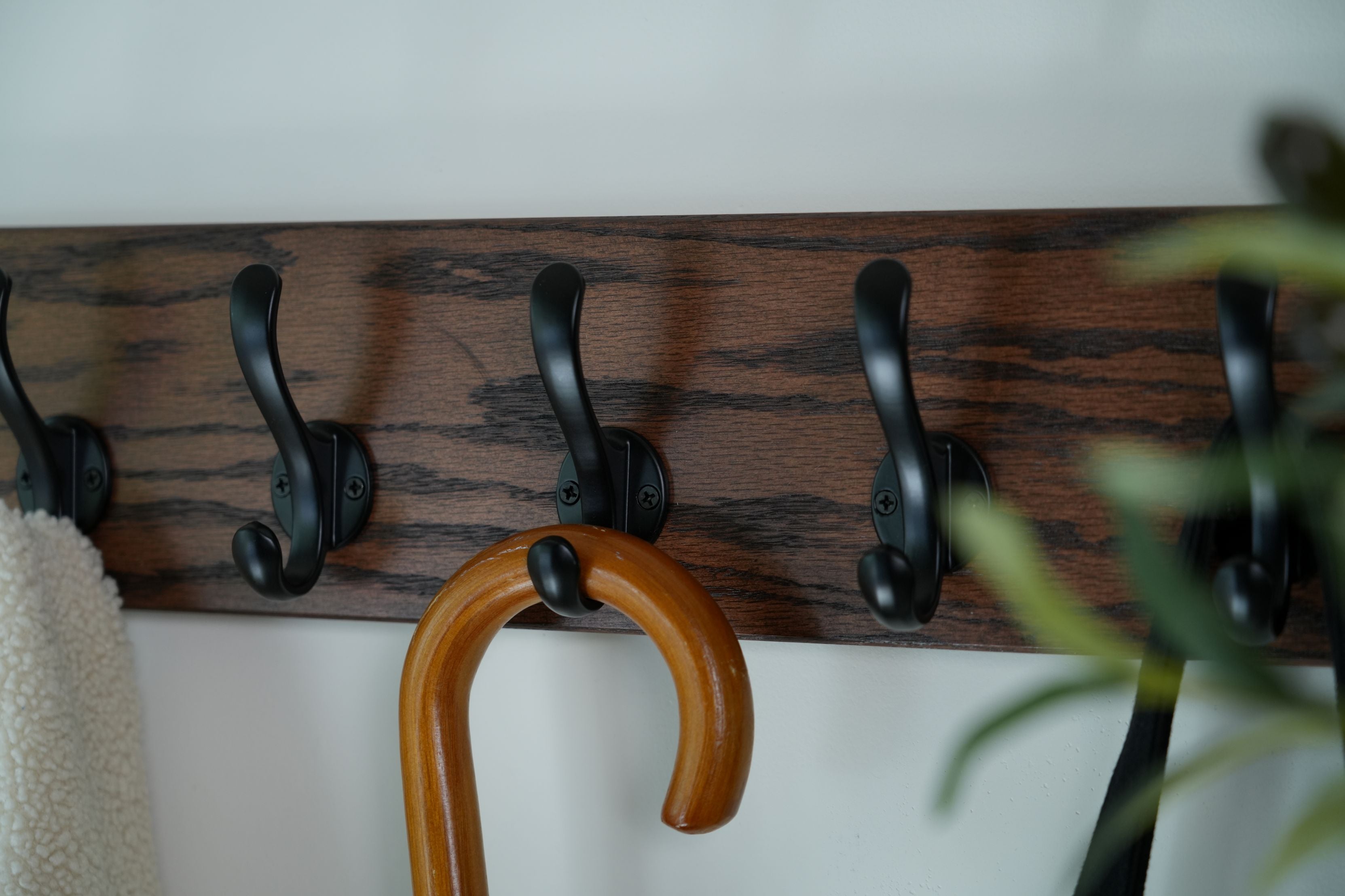 Wooden wall hook rack with black hooks and a brown coat hanger on a white wall.