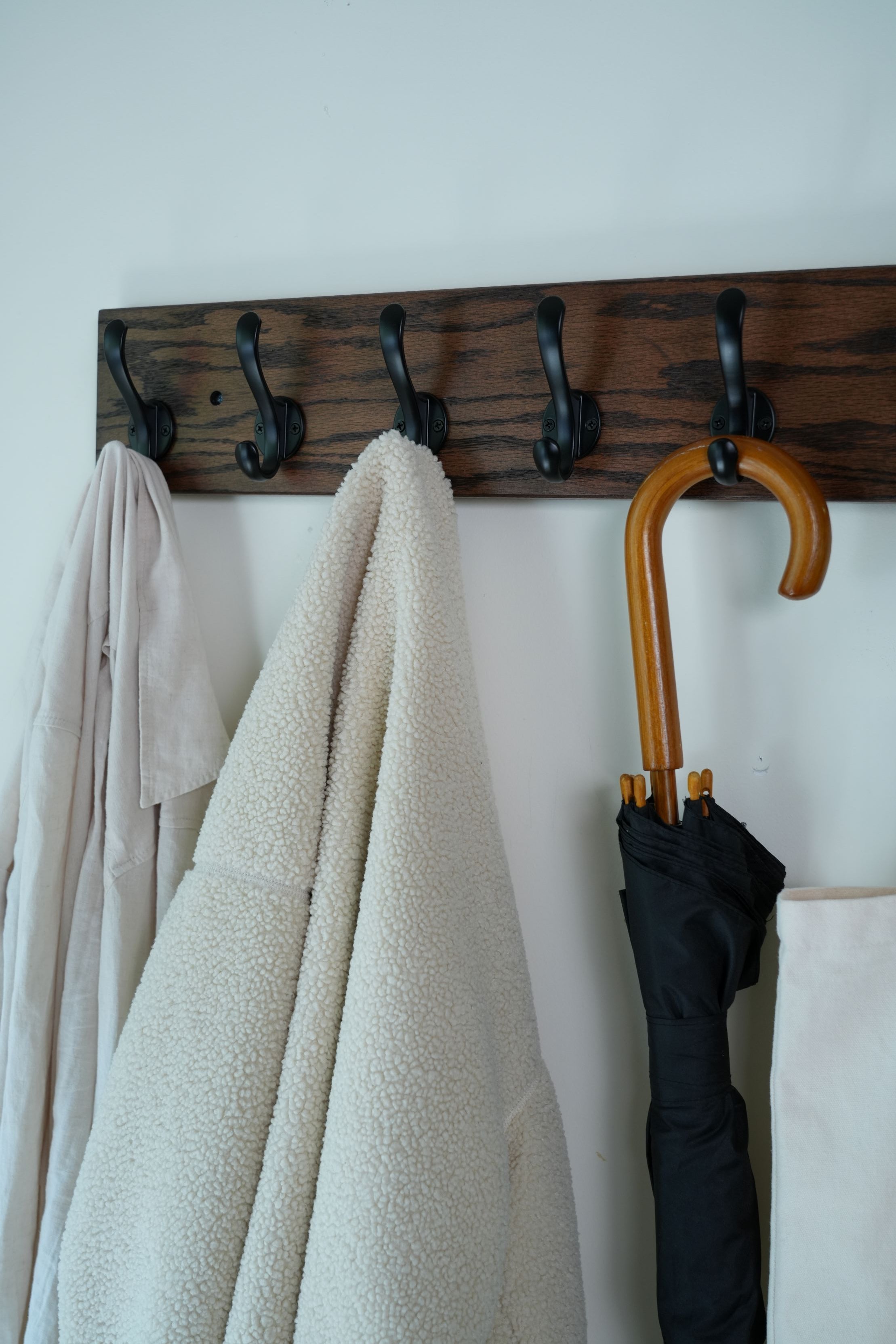 Umbrella stand with folded umbrellas and a black umbrella on a white wall.