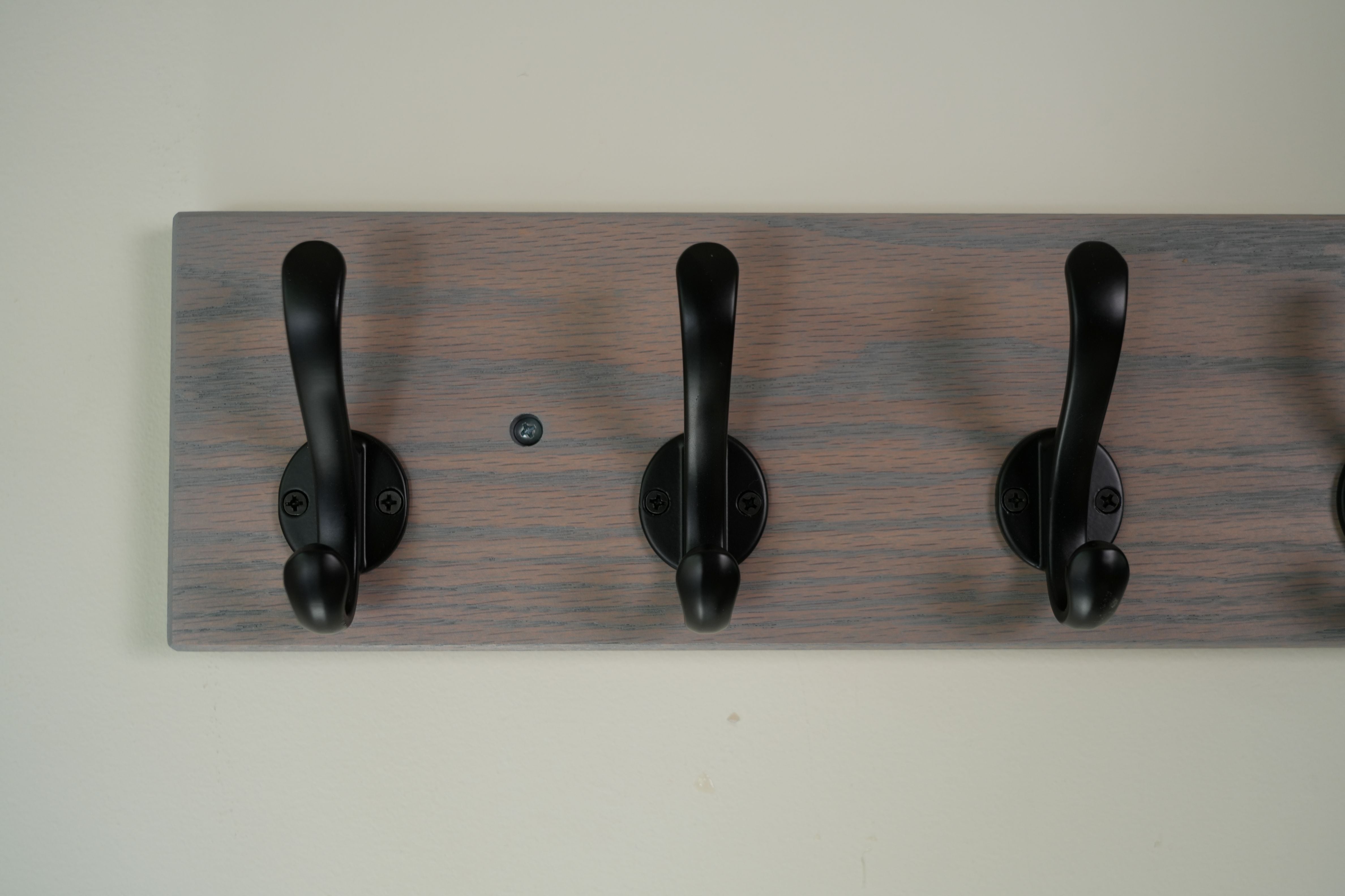 Wooden wall hook with three black hooks on a plain background