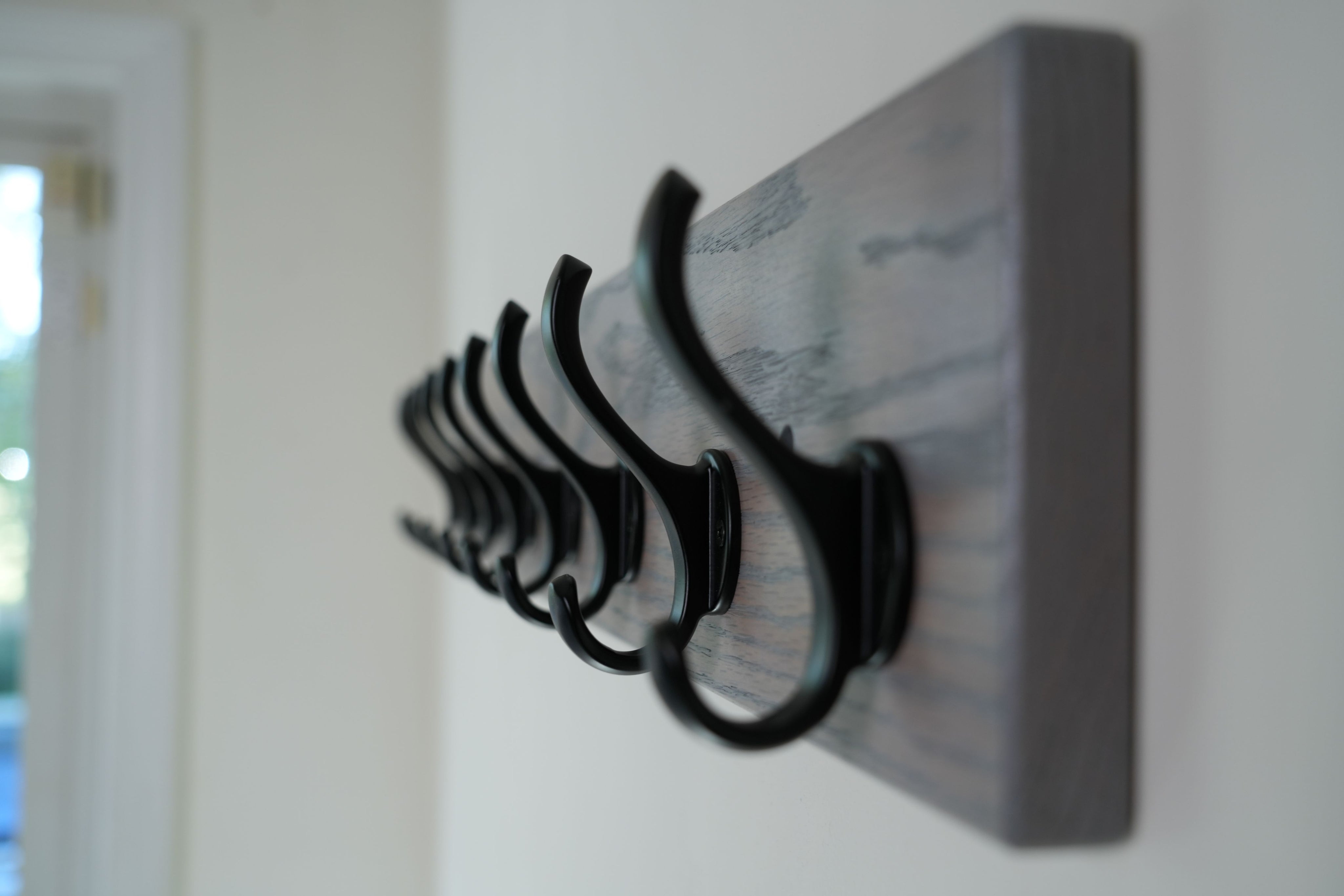 Wooden wall hook rack with black hooks on a white wall.