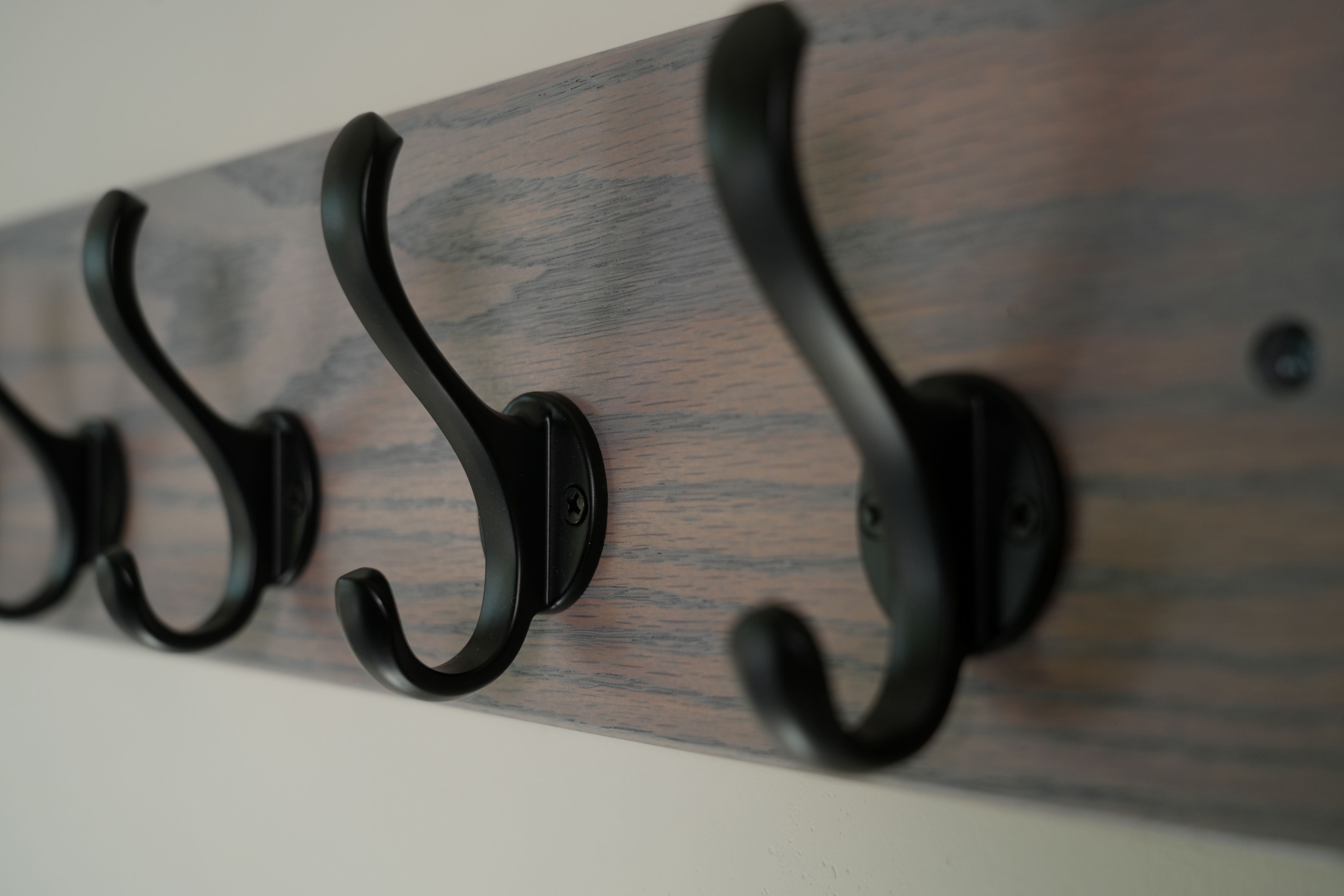 Wooden wall hook with black metal hooks on a plain background
