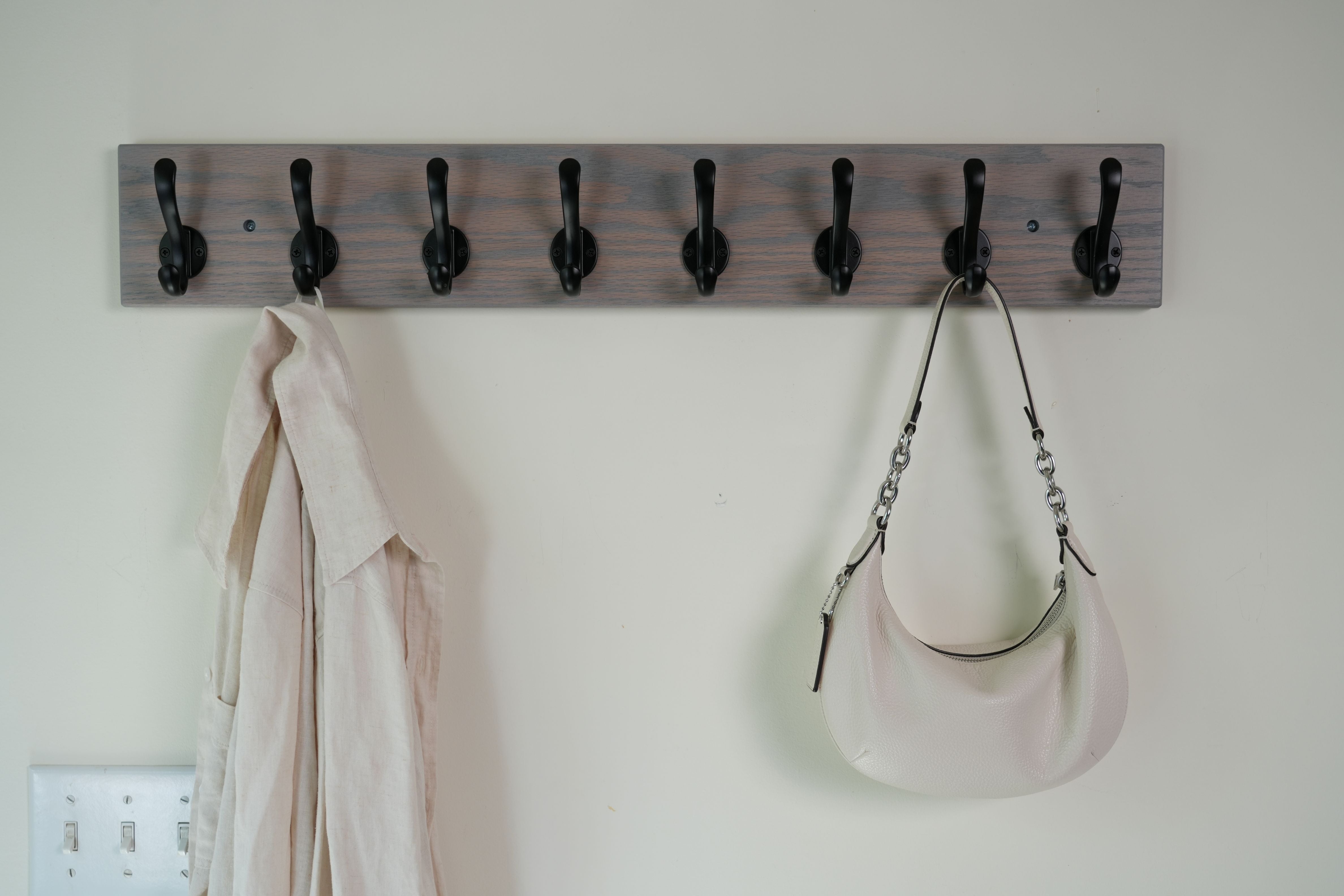 Wooden coat rack with hooks on a white wall, holding a coat and a handbag.