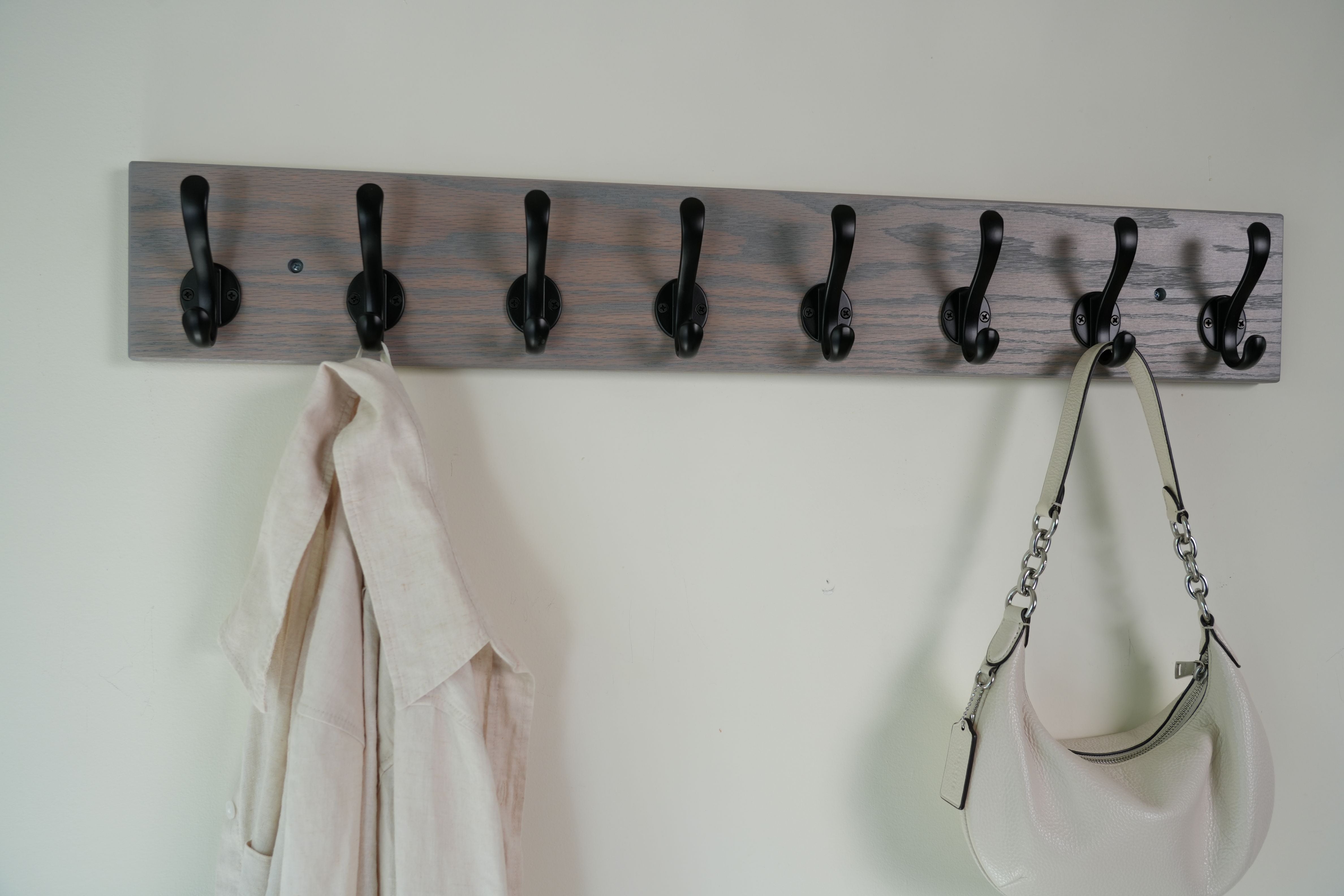 Wooden coat rack with hooks holding a shirt and a handbag against a white wall.