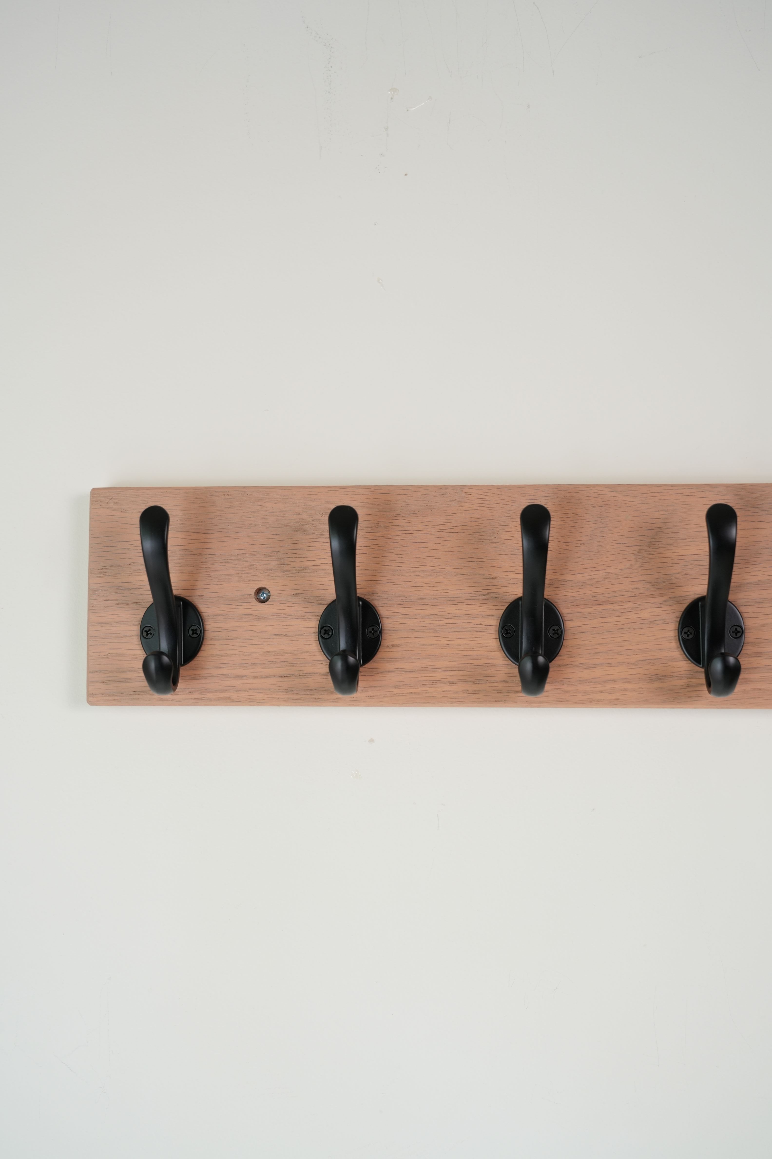 Wooden wall hook rack with four black hooks on a light gray background