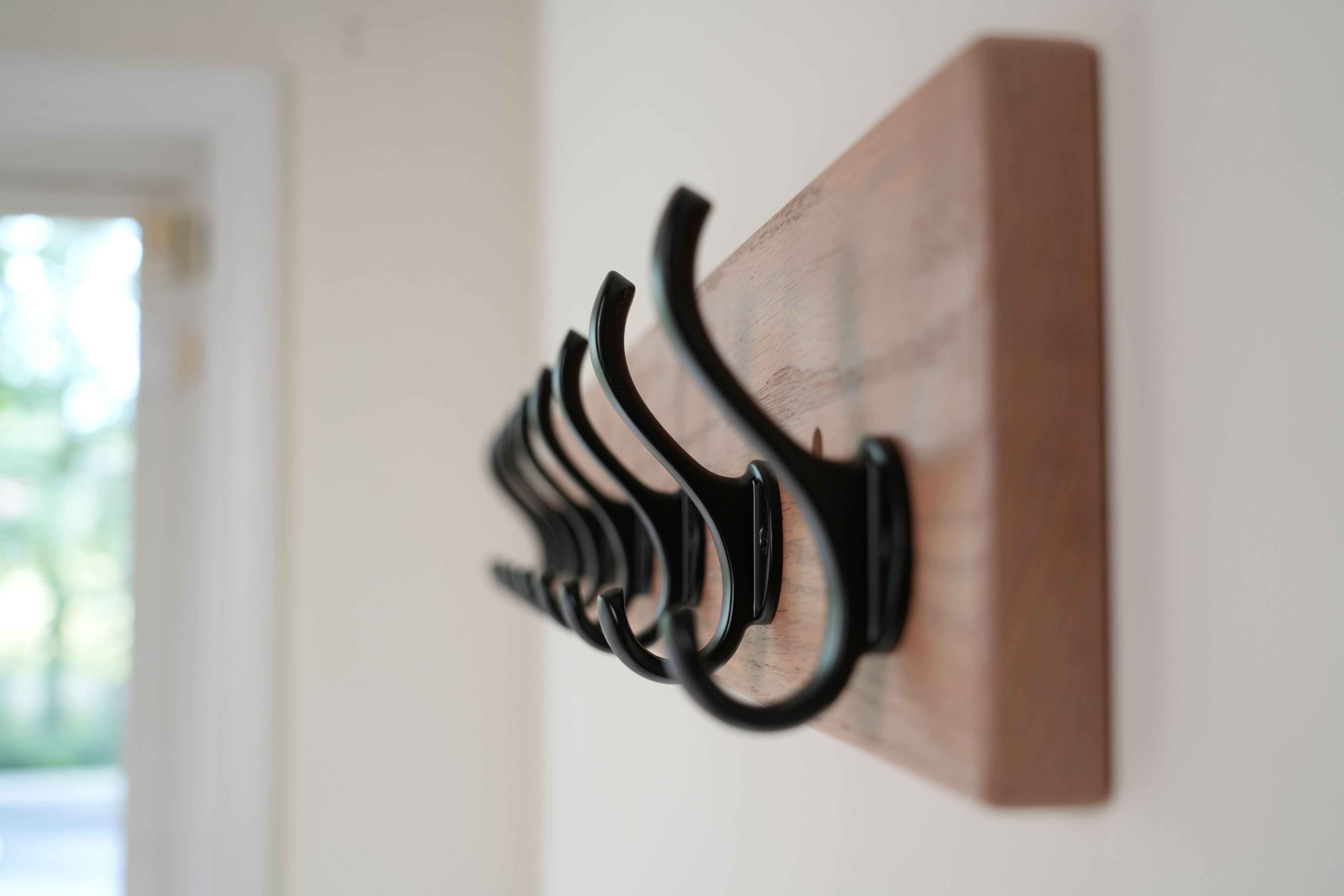 Set of black hooks on a wooden board mounted on a wall.