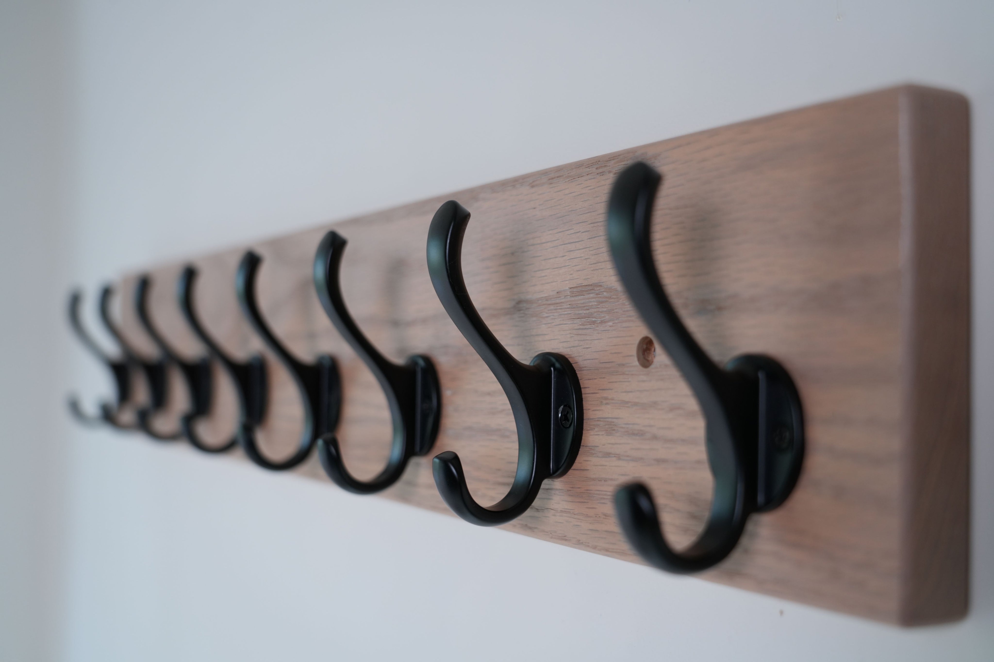 Wooden wall rack with black hooks on a plain background