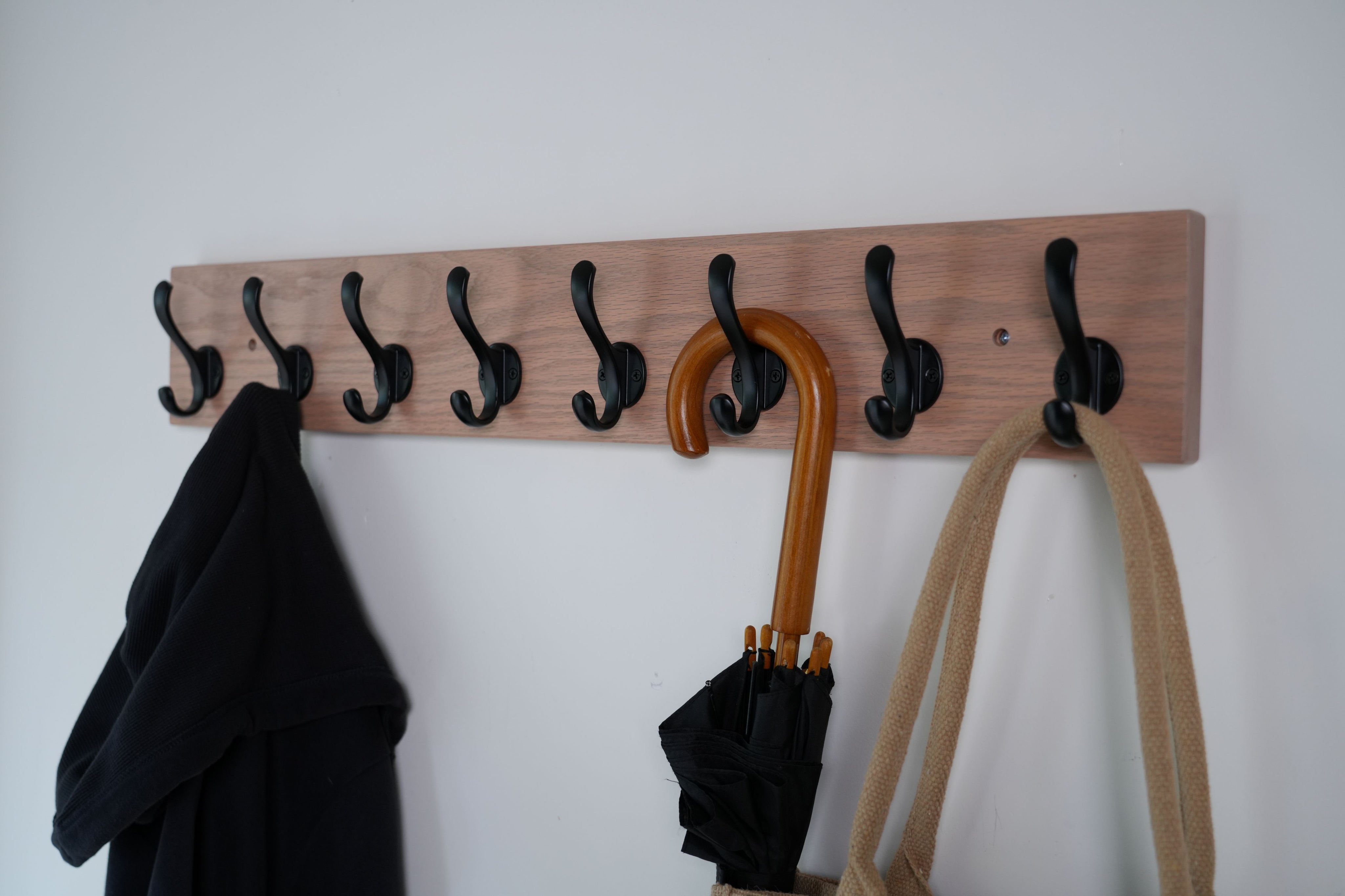 Wooden coat rack with hooks holding a coat, umbrella, and bag against a white wall.