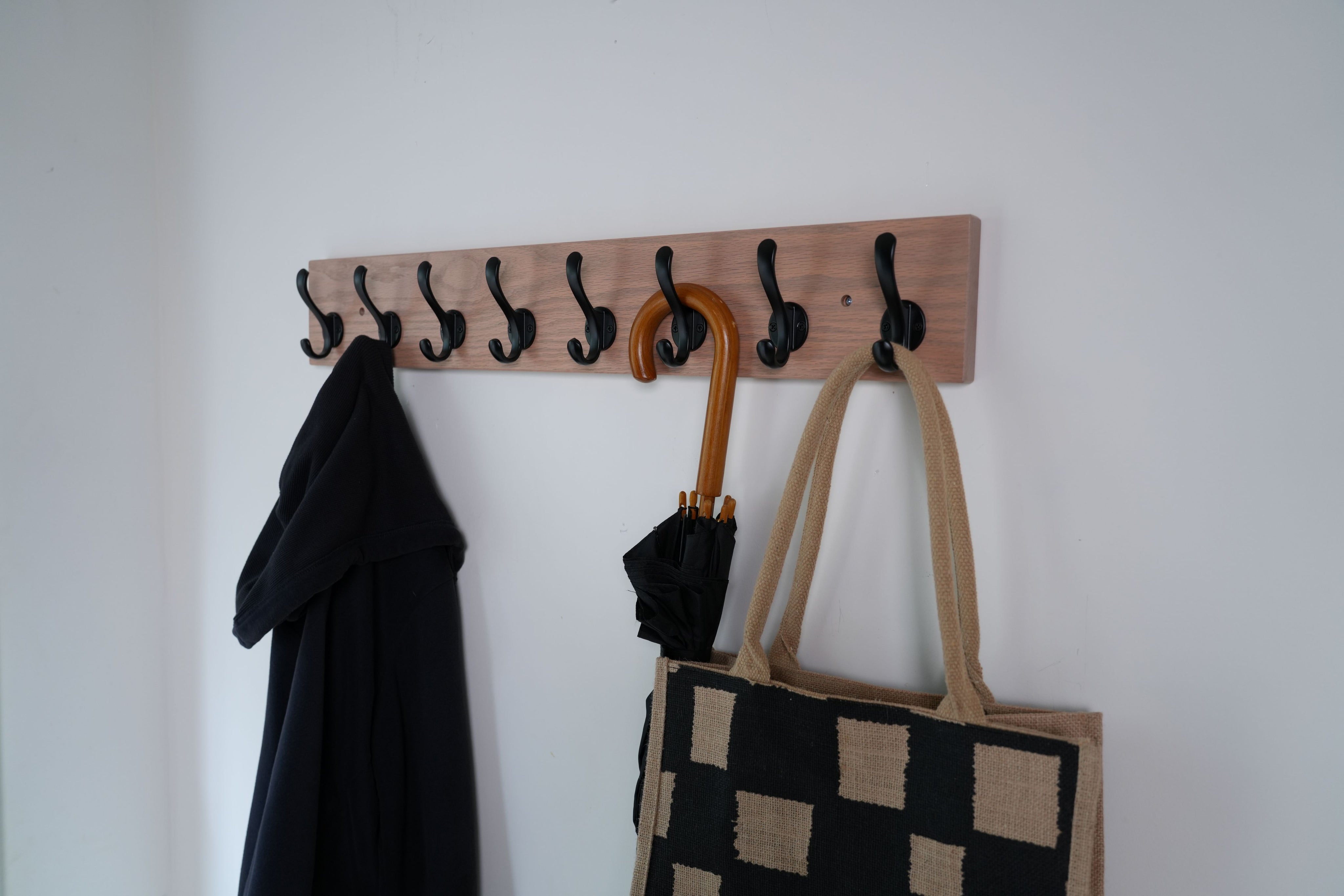 Wooden wall hook with coat, umbrella, and bag on a white wall