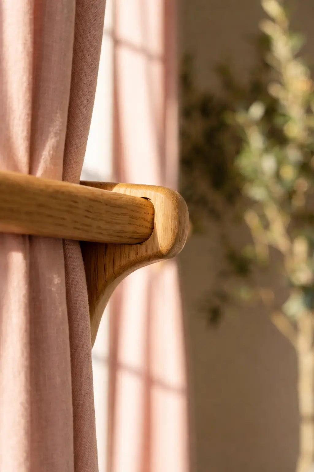Pink curtain with wooden rod and blurred plant in the background