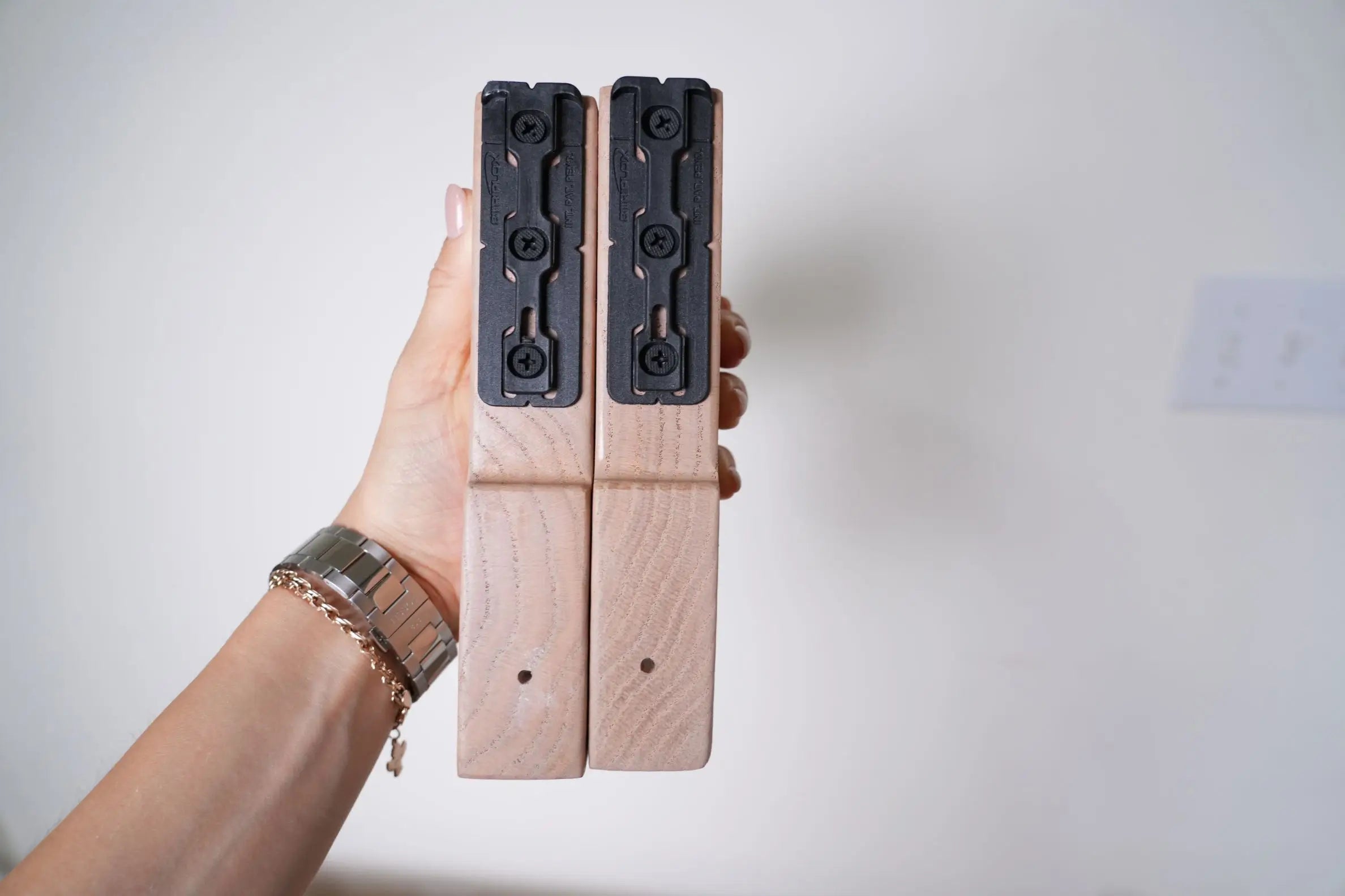 Hand holding two wooden blocks with metal attachments against a plain background