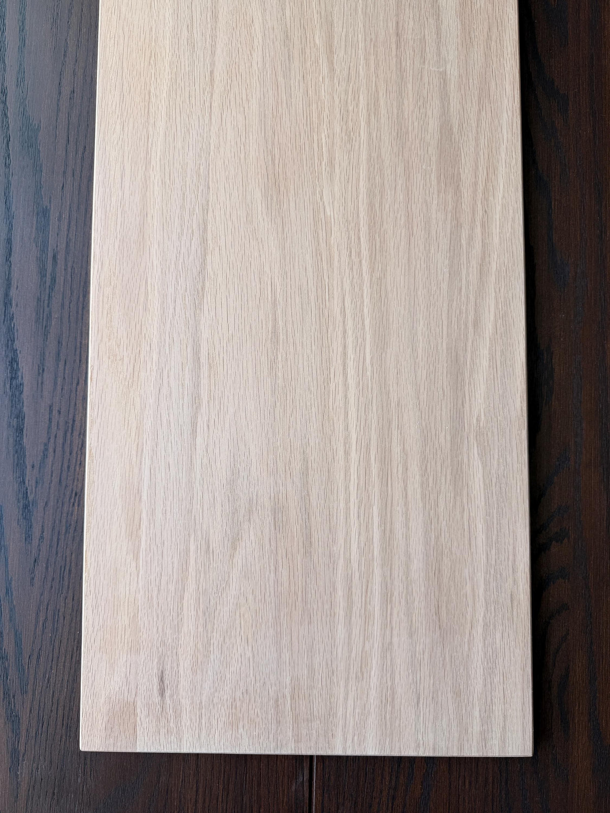 Unfinished oak shelf board on a dark wood floor, sanded smooth and ready to stain or paint