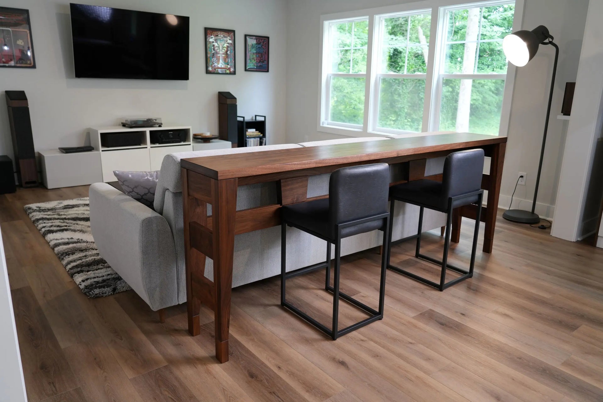 Modern living room with a wooden dining table and chairs, large window, and entertainment setup.