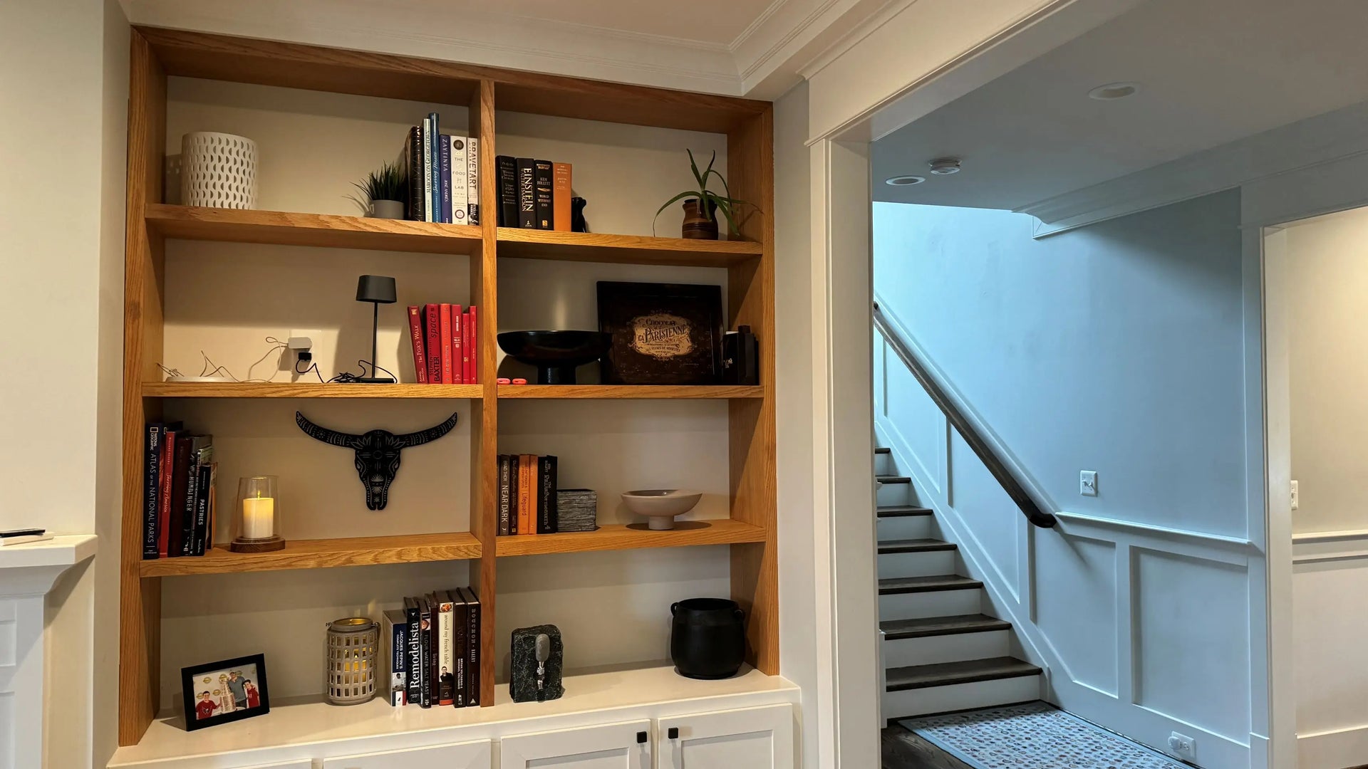 Wooden bookshelf with various items in a room with a staircase.