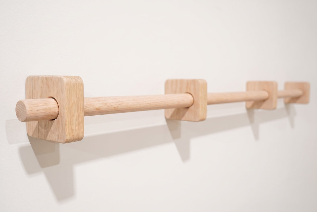 Unfinished oak curtain rod passing through four square brackets on a white wall